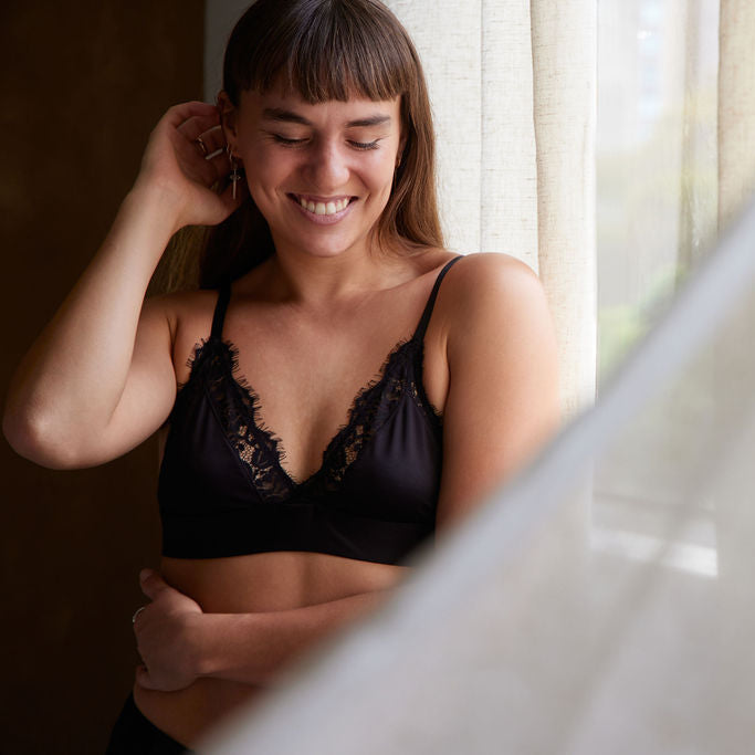 Woman wearing a black lace bra smiling in front of a mirror.