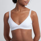 Woman wearing a white Alma bralette against a plain background.