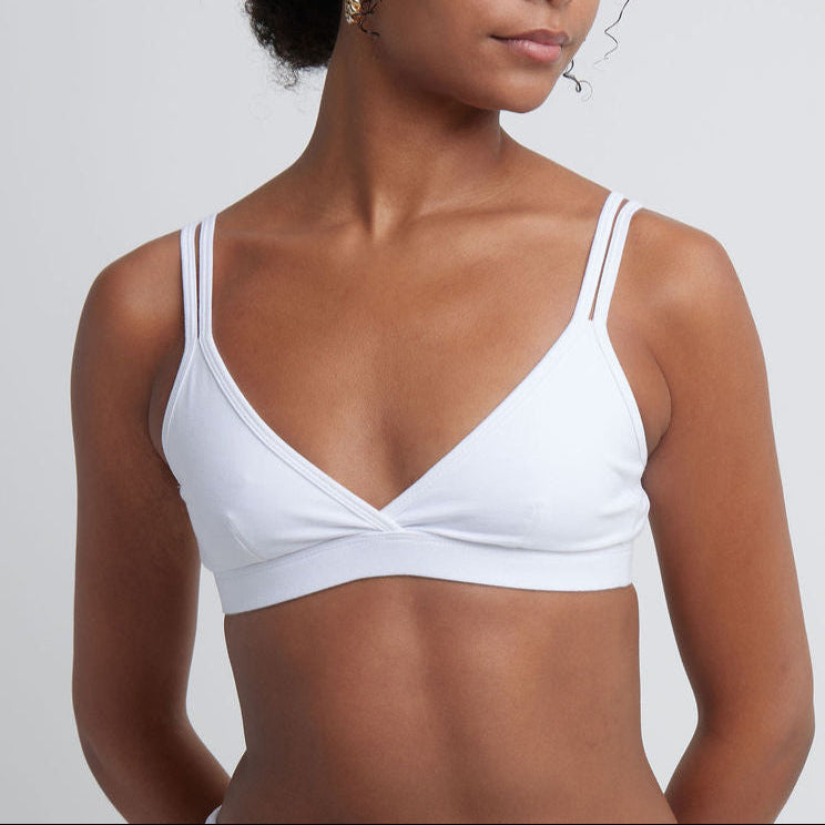 Woman wearing a white Alma bralette against a plain background.