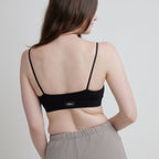 Woman wearing a black Alma bralette with thin straps on a plain background.
