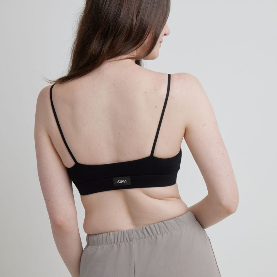 Woman wearing a black Alma bralette with thin straps on a plain background.