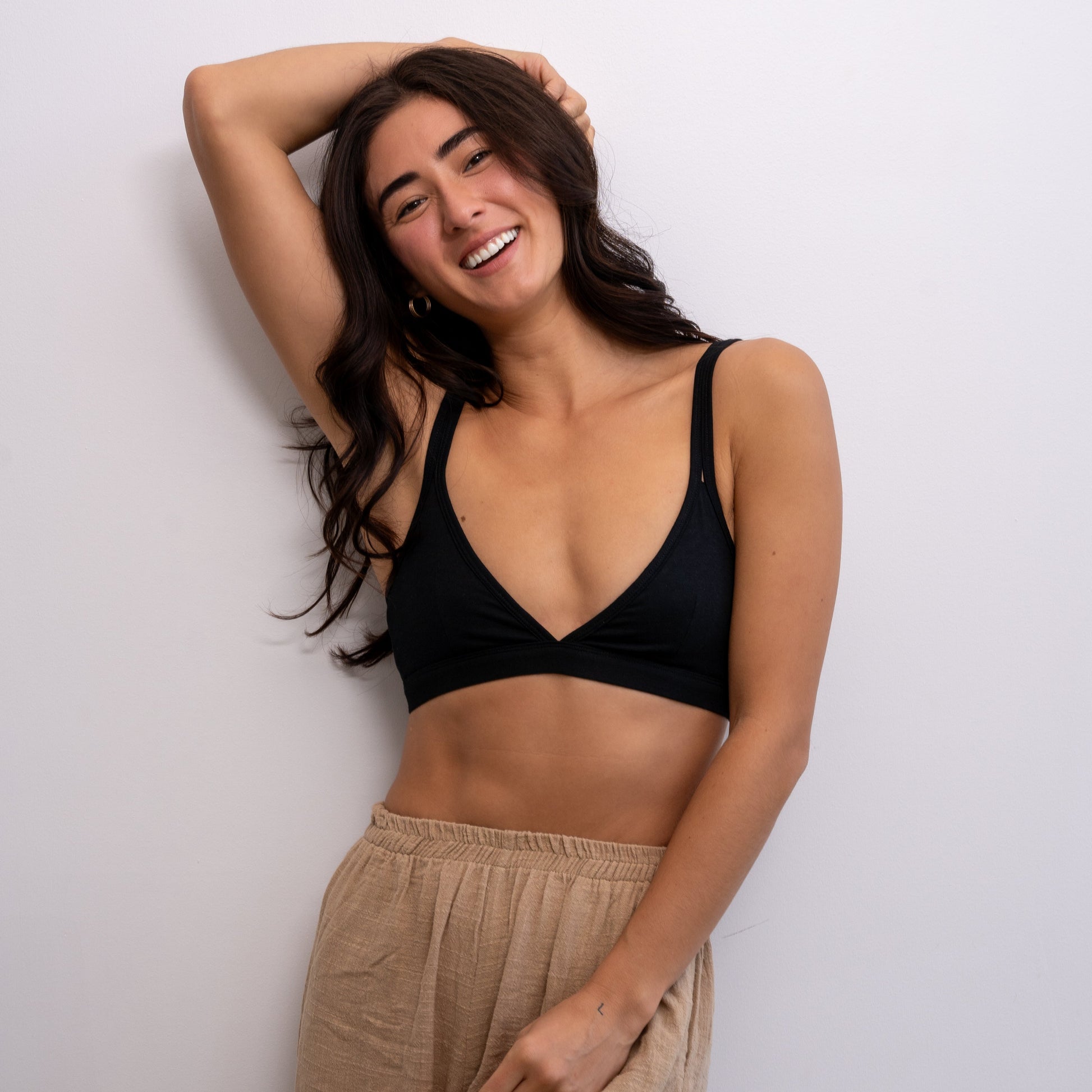 Woman wearing a black Alma bralette and beige pants against a white background.