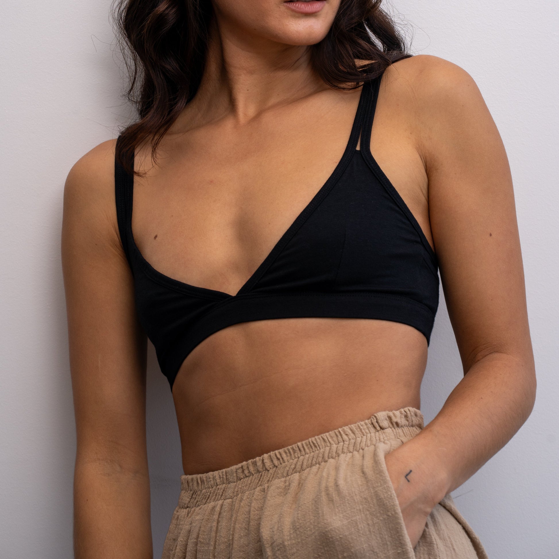 Woman wearing a black Alma bralette and beige pants against a white background.