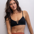 Woman wearing a black Alma bralette and rust-coloured pants against a white background.