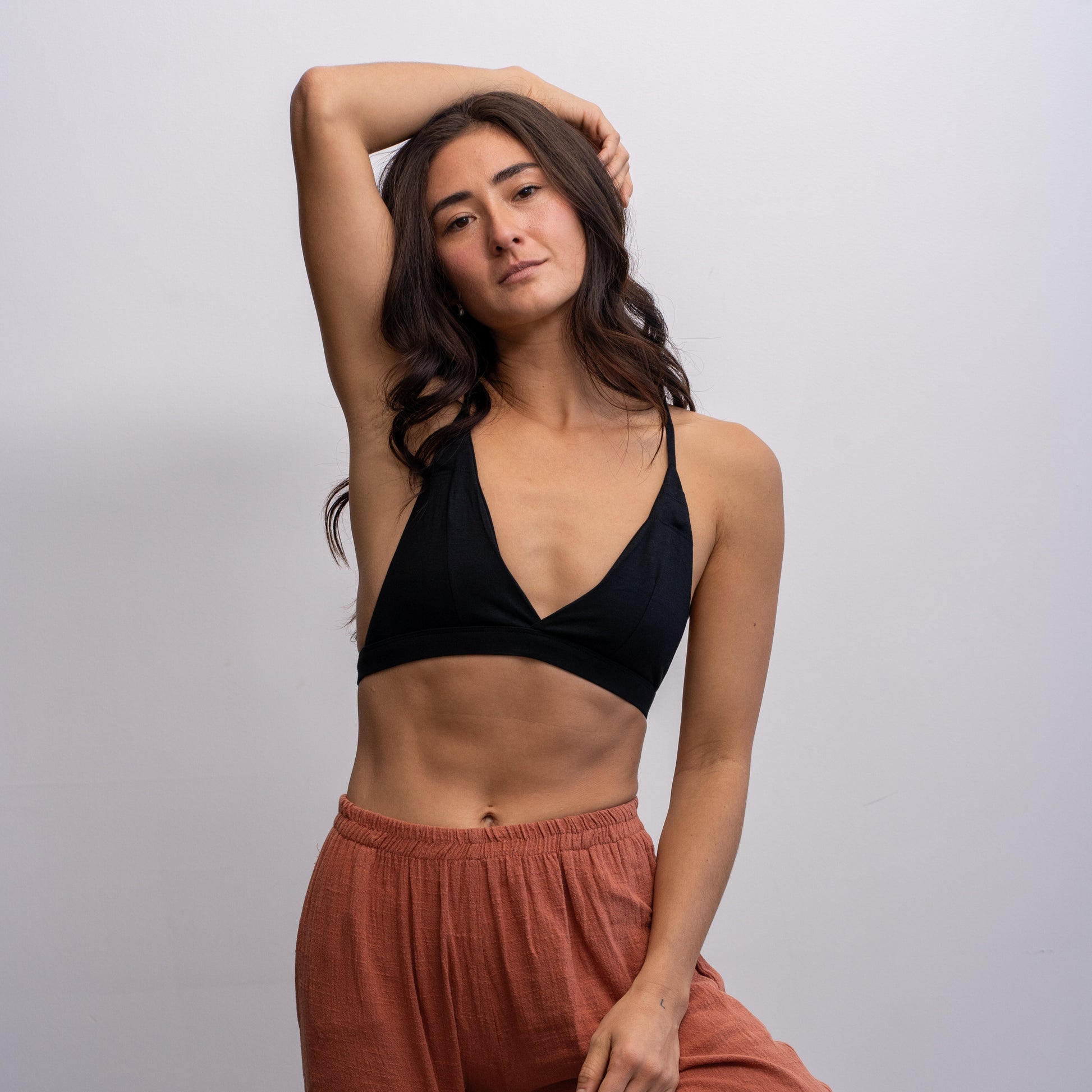 Woman wearing a black Alma bralette and rust-colored pants against a plain background.