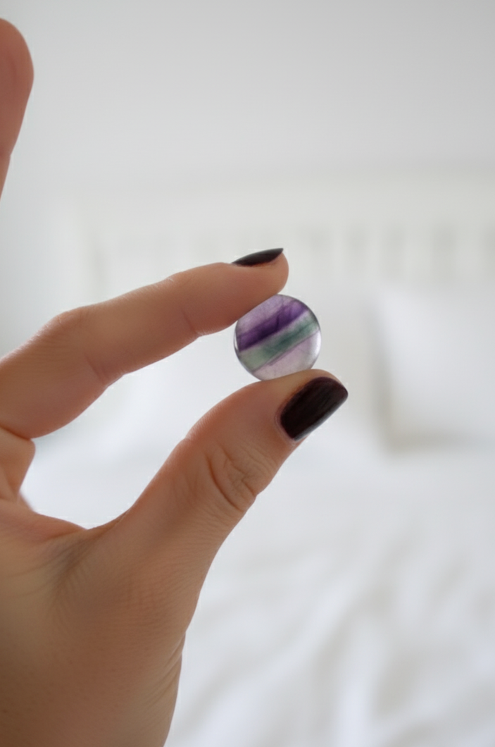 A focused shot of a female's hand holding a small round coloured pocket crystal against a white background.