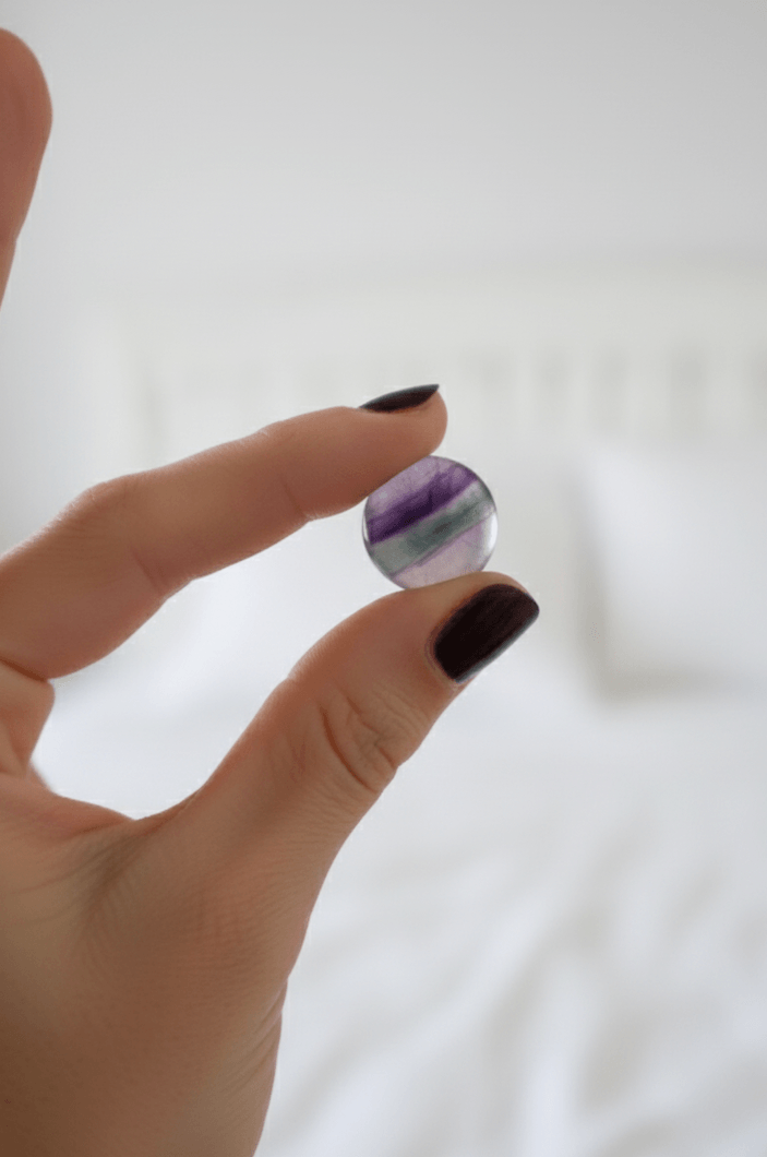 A focused shot of a female's hand holding a small round coloured pocket crystal against a white background.