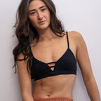 Woman wearing a black Alma bralette and rust-coloured pants against a white background.