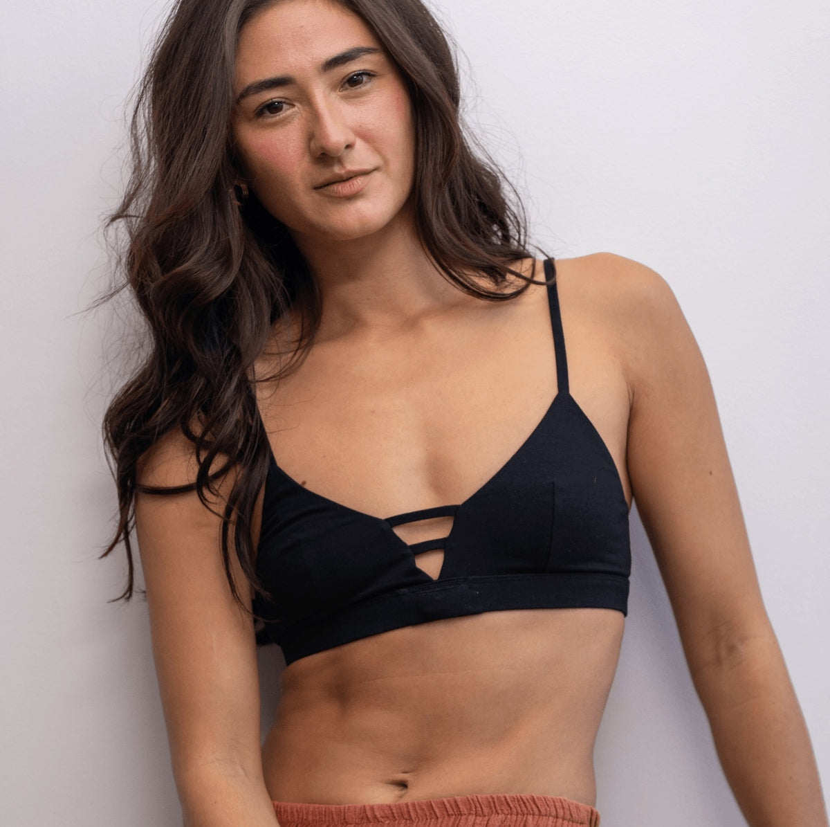 Woman wearing a black Alma bralette and rust-coloured pants against a white background.