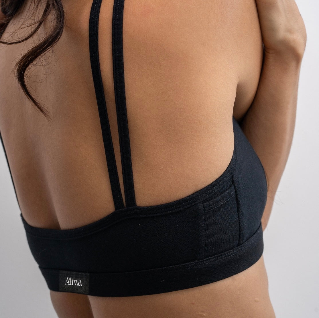 A woman wearing a black Alma bralette, stretching to the side.