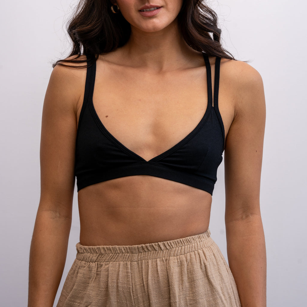 A front shot of a woman wearing a black Alma bralette with beige-coloured trousers.