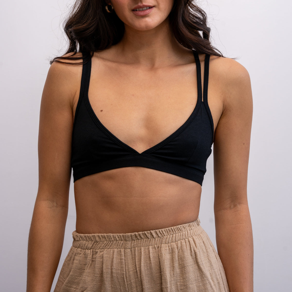 A front shot of a woman wearing a black Alma bralette with beige-coloured trousers.