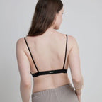 A back shot of a woman wearing a black Alma bralette, which has thin straps and a thin back.