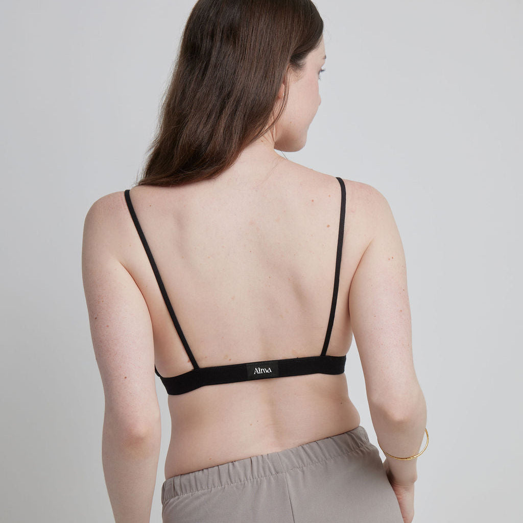 A back shot of a woman wearing a black Alma bralette, which has thin straps and a thin back.