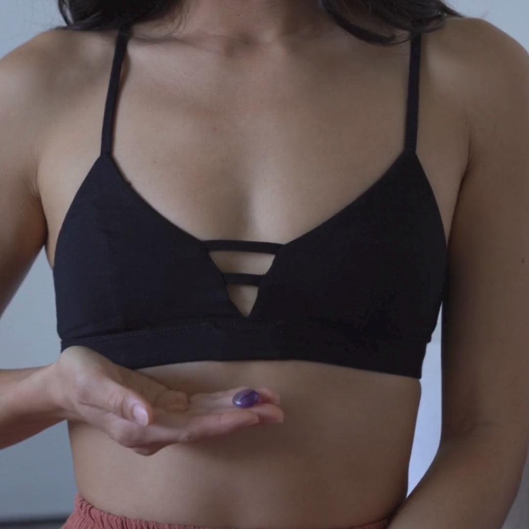 A woman wearing a Calia Alma bralette and placing a pocket crystal into a subtle pocket at the heart-centre.